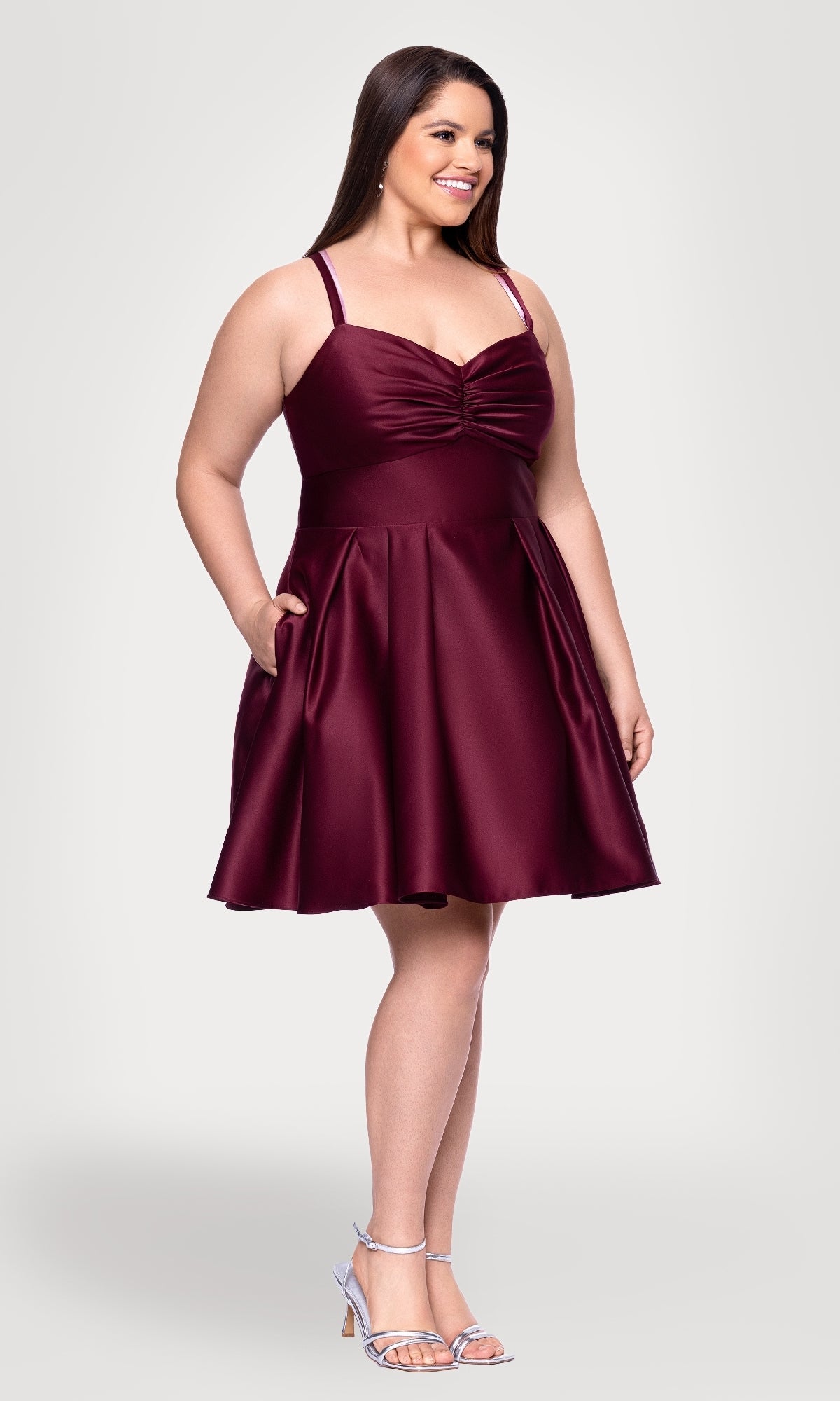 A woman wears the Plus Short Wine Hoco Dress: Blondie Nites 4927BNW, a sleeveless, knee-length cocktail dress with a fitted bodice and flared skirt, paired with silver heels against a plain light background.